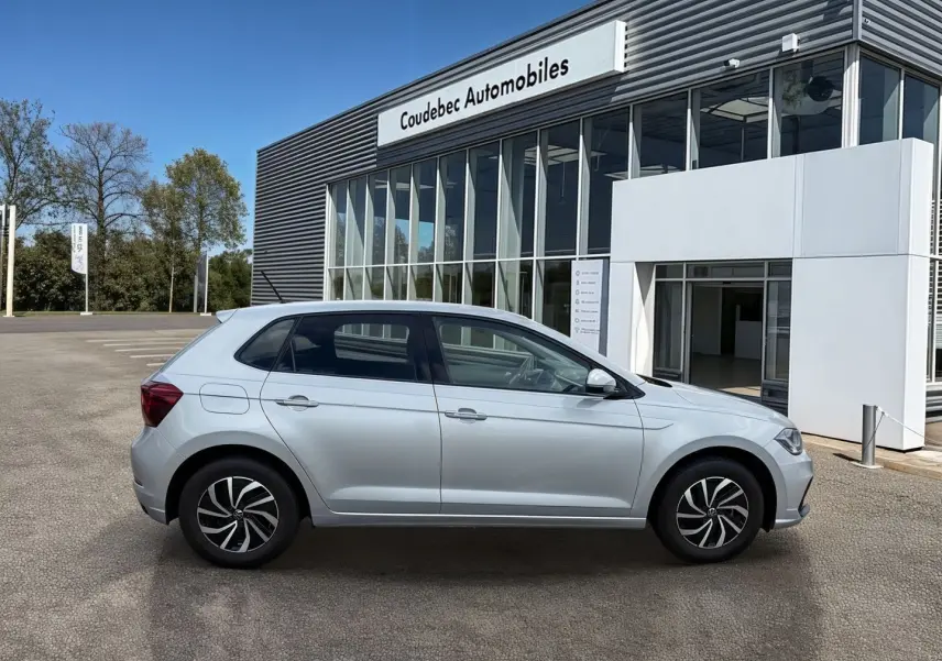 Profil côté droit de la Volkswagen Polo grise 2025 avec jantes alliage, stationnée devant un showroom moderne.