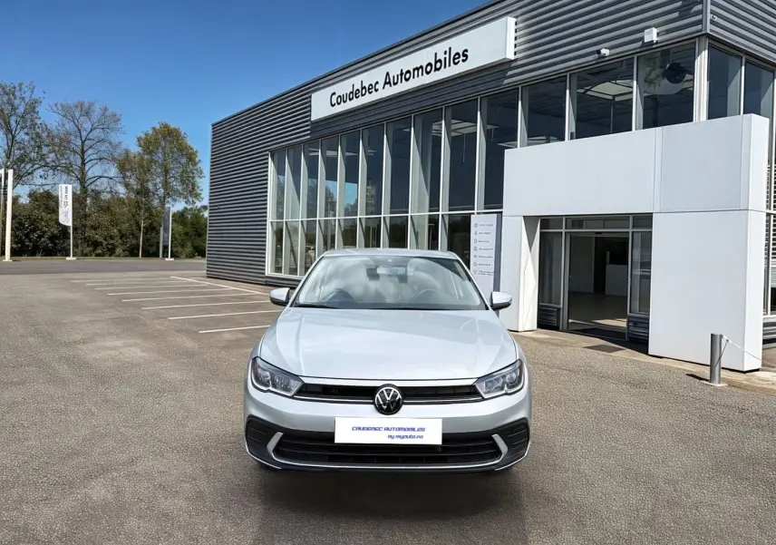 Vue de face d'une Volkswagen Polo grise 2025 avec feux LED, stationnée devant un bâtiment de concession automobile.