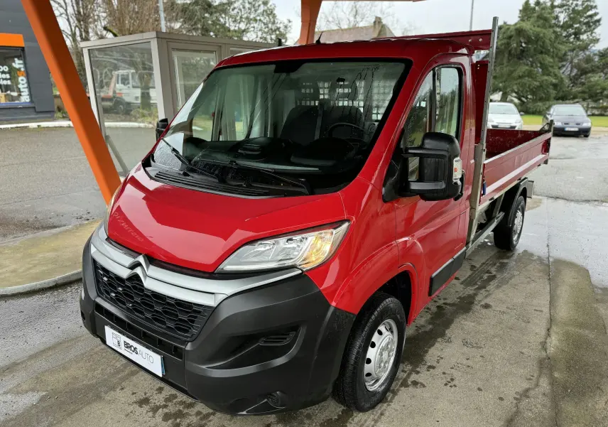 Vue 3/4 avant droite d'un utilitaire Citroën Jumper benne rouge avec ridelles métalliques et jantes acier 15 pouces.