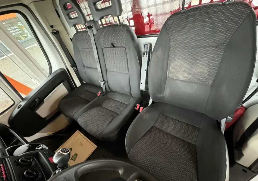 Vue intérieure du poste de conduite du Citroën Jumper rouge, montrant les sièges tissu noir et la boîte manuelle.