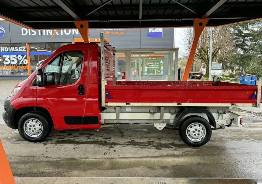 Profil droit d'un utilitaire Citroën Jumper benne rouge de 2019 avec ridelles et jantes acier 15 pouces sous abri.