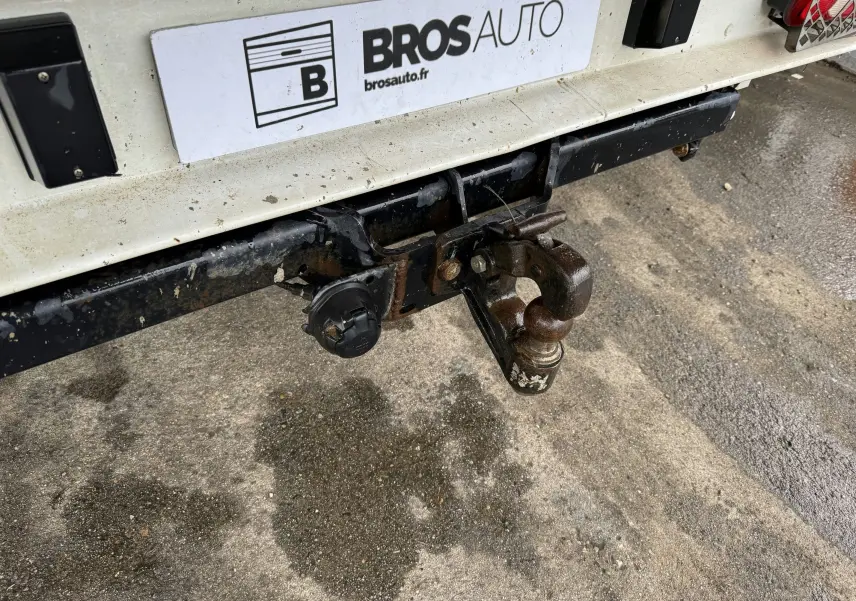 Gros plan sur l'attelage arrière rouillé du Citroën Jumper benne rouge, avec plaque d'immatriculation Bros Auto visible.