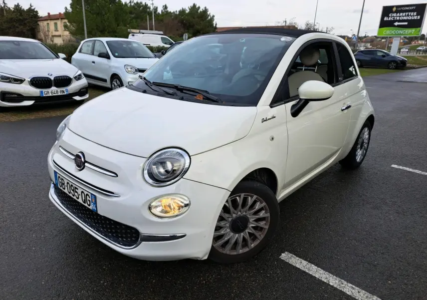 Fiat 500 Cabriolet blanche vue en 3/4 avant droit, toit ouvert partiellement, phare avant droit allumé sur parking.