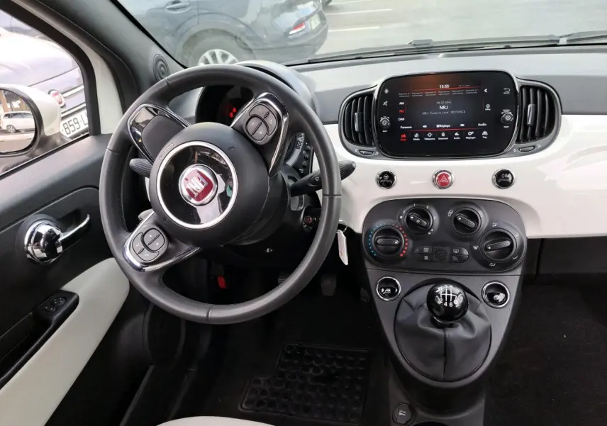 Intérieur de Fiat 500 Cabriolet blanc 2021, vue du poste de conduite avec volant, tableau de bord et levier de vitesses manuel.