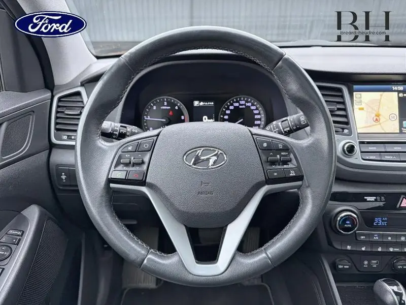 Vue intérieure centrée sur le volant cuir noir Hyundai Tucson 2018 avec tableau de bord et écran tactile GPS visible.
