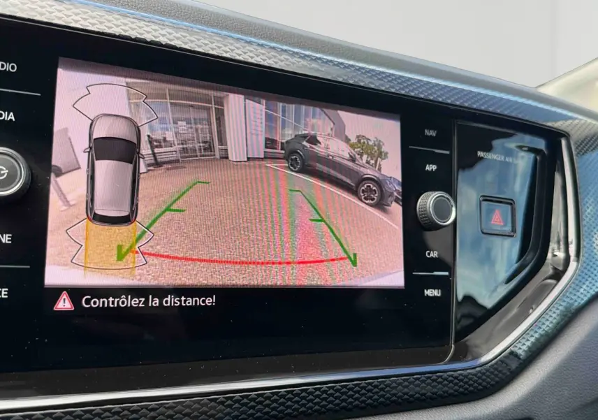 Écran tactile intérieur montrant la caméra de recul avec vue arrière d'une Volkswagen Polo grise stationnée.