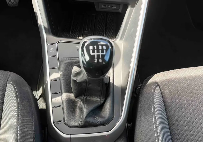 Gros plan sur le levier de vitesses manuel noir de la Volkswagen Polo grise, entouré des sièges avant en tissu gris.