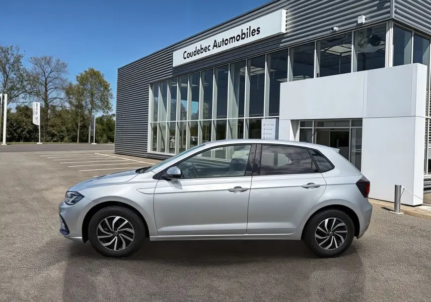 Profil droit d'une Volkswagen Polo grise 2025 stationnée devant un bâtiment moderne de concession automobile.