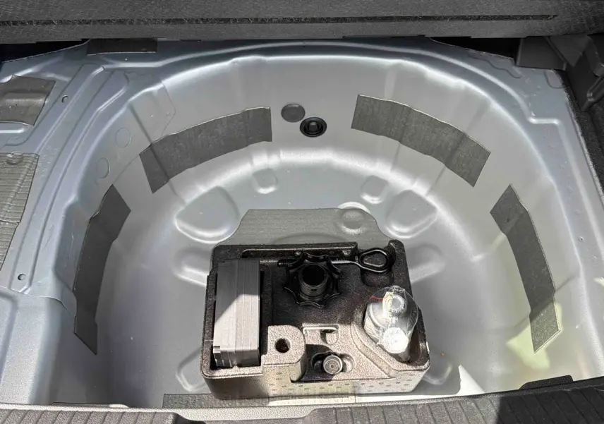 Vue plongeante sur le coffre ouvert d'une Volkswagen Polo grise, montrant le rangement pour roue de secours et outils.