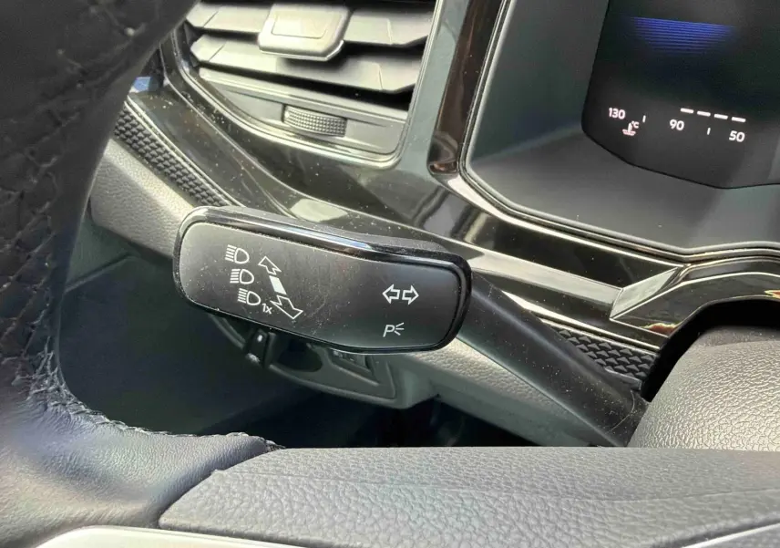 Gros plan sur la manette de clignotants noire et le tableau de bord digital d'une Volkswagen Polo grise, vue côté conducteur.