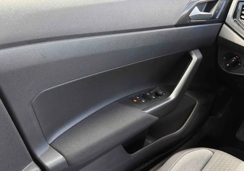 Détail de la portière côté conducteur grise avec commandes électriques des vitres et rétroviseur dans une Volkswagen Polo 2025.