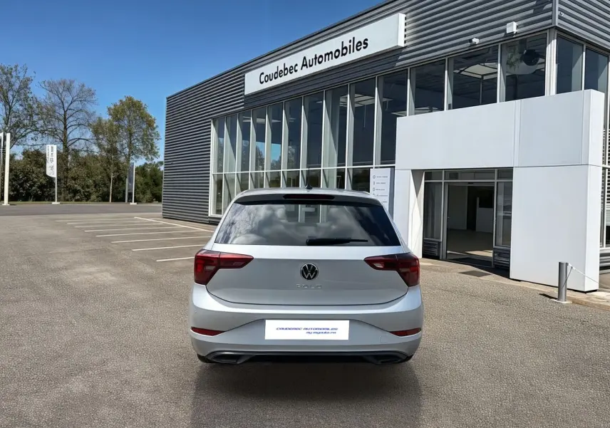 Vue arrière d'une Volkswagen Polo grise 2025 garée devant un bâtiment moderne de concession automobile.