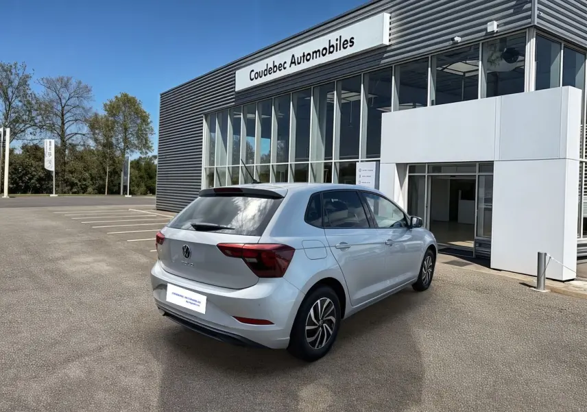 Volkswagen Polo grise vue 3/4 arrière droit, stationnée devant un bâtiment de concession Coudebec Automobiles.
