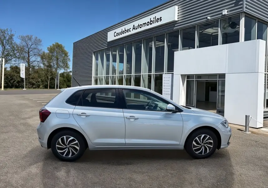 Profil côté gauche d'une Volkswagen Polo grise 2025 garée devant un bâtiment moderne de concession automobile.