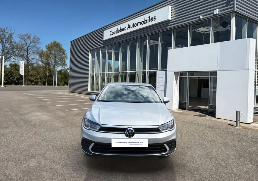 Vue avant d'une Volkswagen Polo grise 2025 stationnée devant un bâtiment commercial moderne.