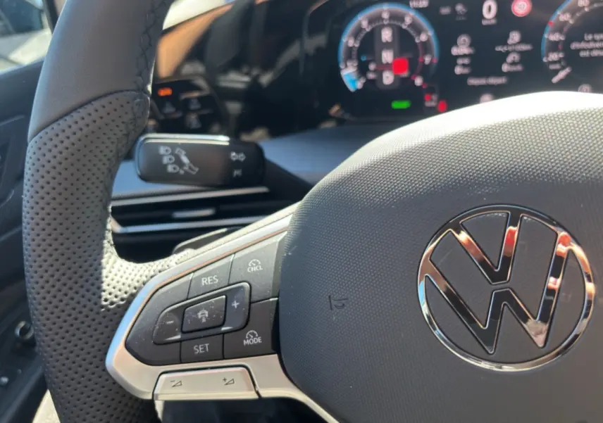 Gros plan sur le volant cuir multifonctions de la Volkswagen Golf TDI 150 R-Line 2026 avec affichage numérique en arrière-plan.