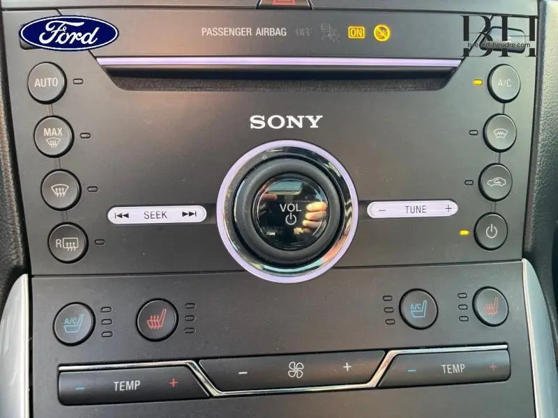 Gros plan sur la console centrale noire du Ford Edge 2016 avec commandes Sony et réglages climatisation visibles.