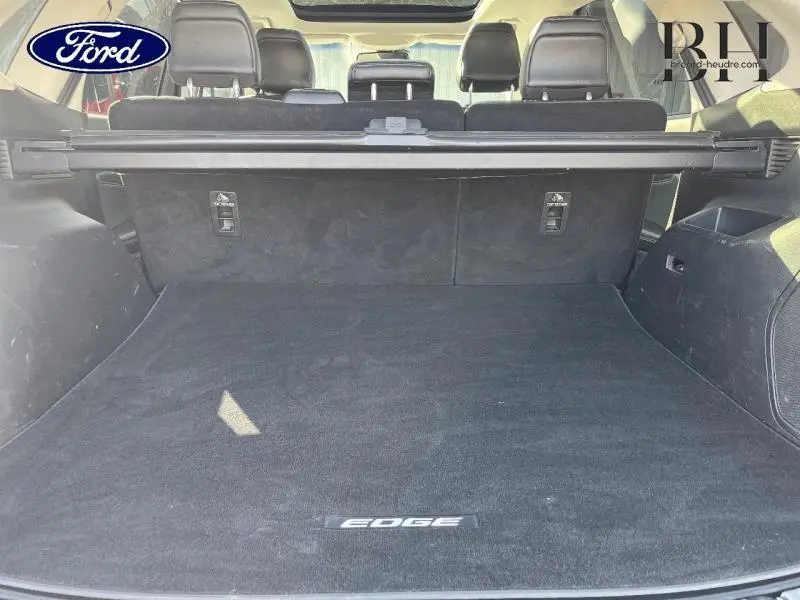 Coffre ouvert du Ford Edge blanc Platinum, vue arrière montrant la moquette avec logo EDGE et sièges en cuir noir.