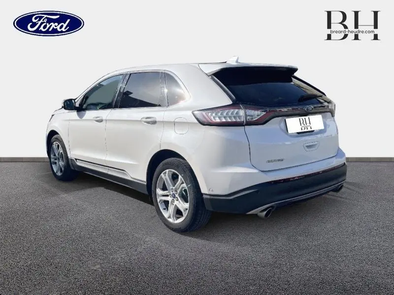 Vue 3/4 arrière droite d'un Ford Edge blanc Platinum avec vitres teintées et jantes alu sur fond neutre.