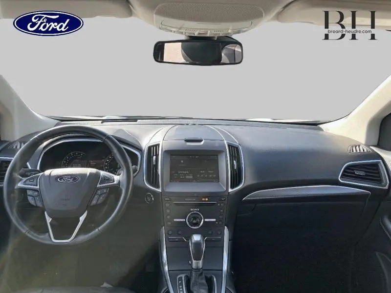 Vue intérieure avant du Ford Edge 2016, tableau de bord noir avec écran tactile central et volant cuir multifonctions.