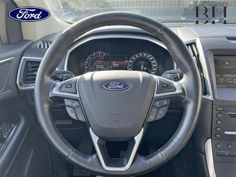 Vue rapprochée du volant en cuir noir du Ford Edge 2016 avec commandes intégrées et tableau de bord visible.