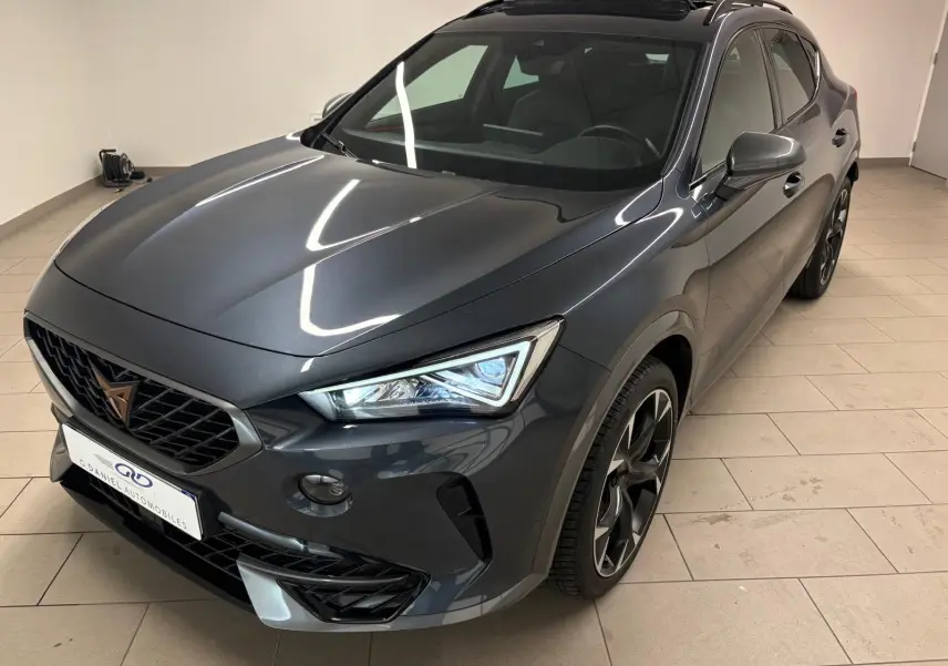 SUV CUPRA Formentor gris magnétique vu en 3/4 avant droit, avec phares allumés et jantes noires distinctives.
