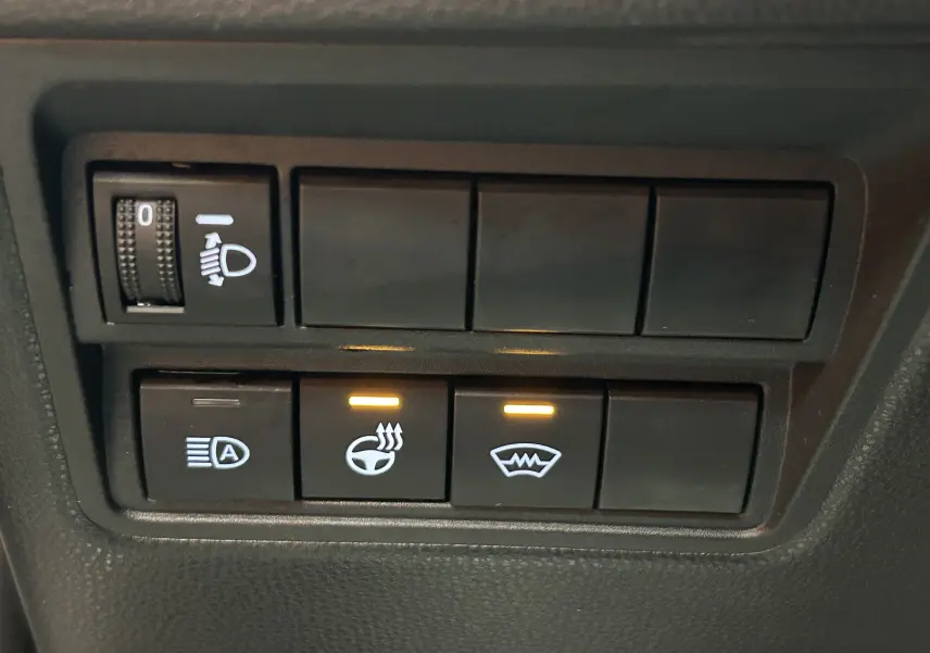 Gros plan sur les boutons de commande du volant chauffant et pare-brise chauffant dans une Toyota Yaris Cross gris minéral.