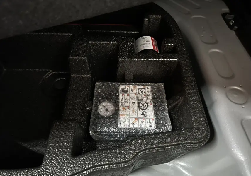 Vue rapprochée du compartiment de rangement dans le coffre d'une Toyota Yaris Cross gris minéral, montrant un kit de réparation pneus.