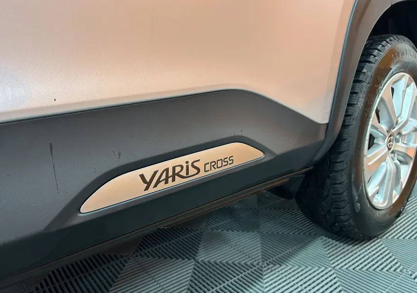 Gros plan sur le bas de caisse côté droit gris minéral d'une Toyota Yaris Cross avec logo et roue avant visible.