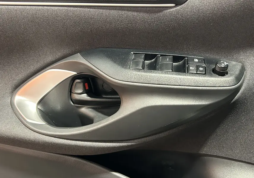 Gros plan sur la poignée intérieure et les commandes de fenêtre côté conducteur d'une Toyota Yaris Cross gris minéral.