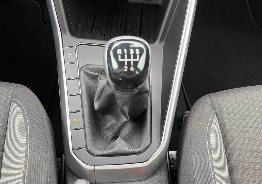 Vue rapprochée du levier de vitesses manuel noir entouré des sièges tissu gris dans une Volkswagen Polo 2025.