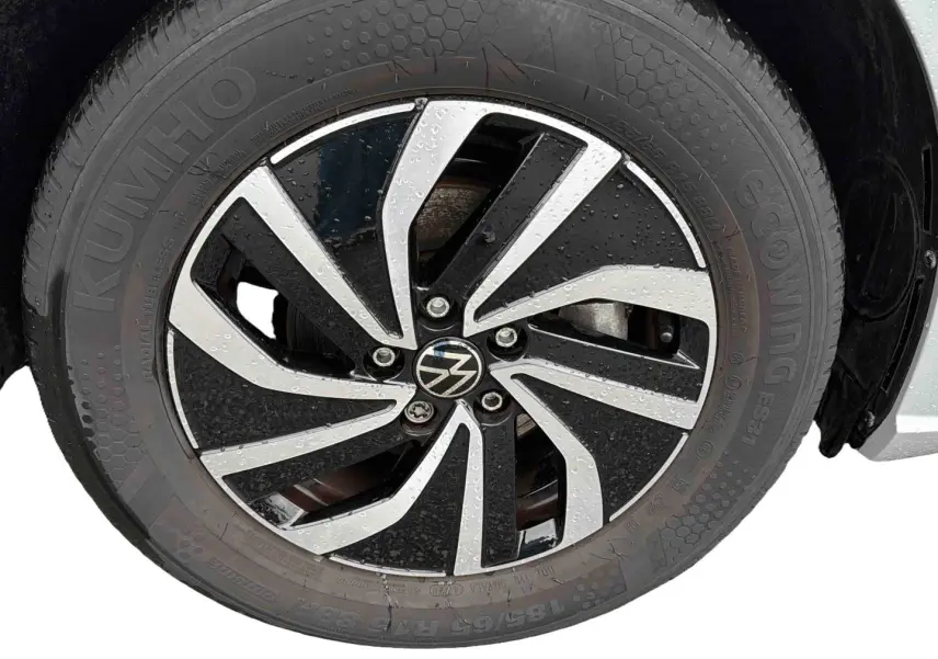 Gros plan sur la jante alliage 15 pouces bicolore avec logo Volkswagen sur pneu Kumho, véhicule gris visible en arrière-plan.