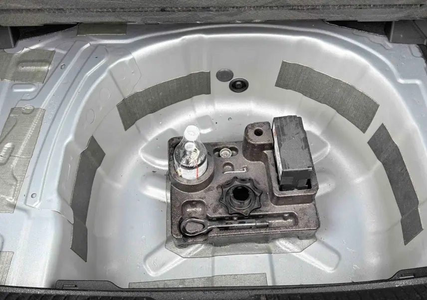 Vue plongeante sur le coffre ouvert d'une Volkswagen Polo grise, montrant le logement de la roue de secours vide avec outils.
