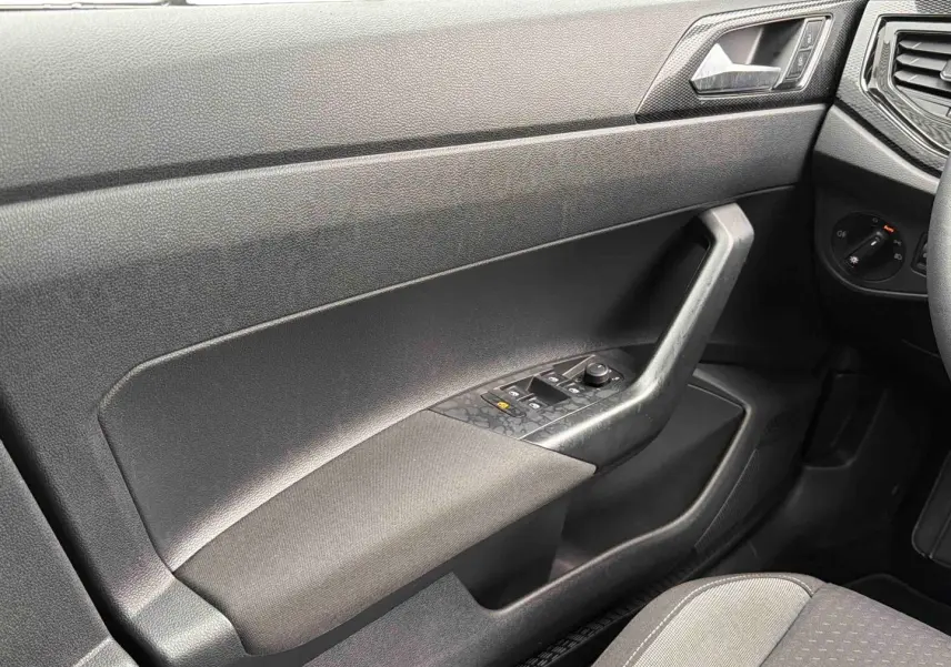 Vue intérieure côté gauche de la porte conducteur grise de la Volkswagen Polo 2025 avec commandes de vitres et tissu noir.