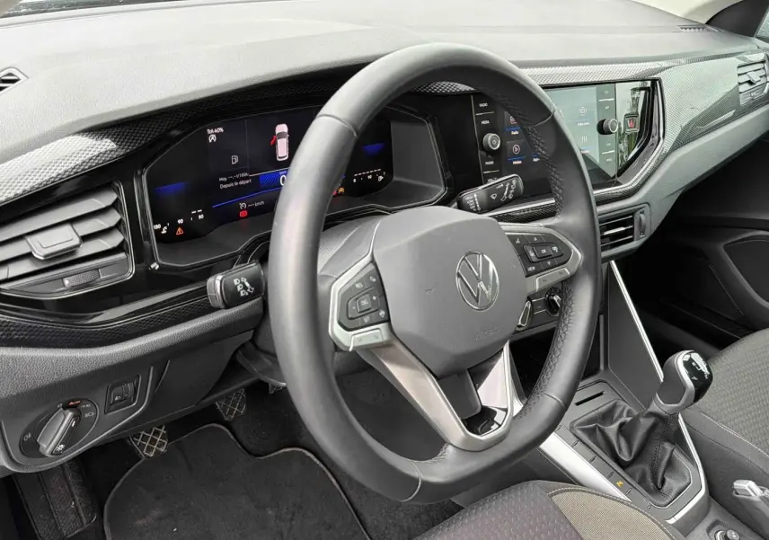 Vue intérieure du poste de conduite de la Volkswagen Polo grise, avec volant multifonctions et levier de vitesse manuel visible.