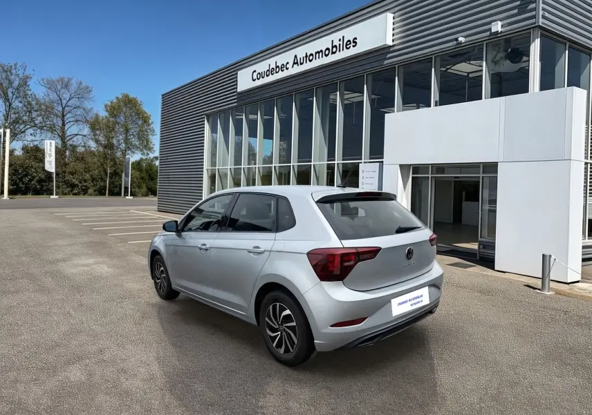 Volkswagen Polo grise vue 3/4 arrière droit, avec vitres surteintées et jantes alliage 15 pouces devant un concessionnaire.