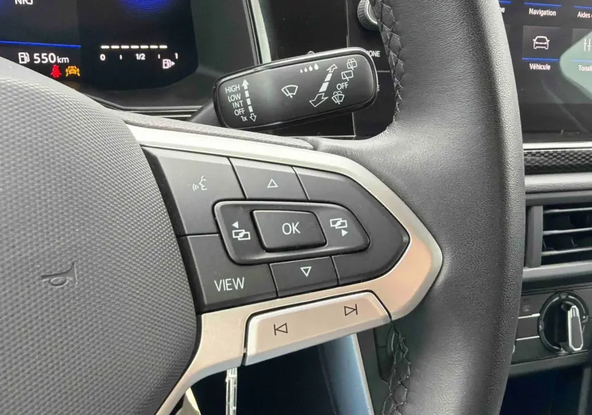 Gros plan sur les commandes gauche du volant noir de la Volkswagen Polo 2025 avec affichage digital en arrière-plan.