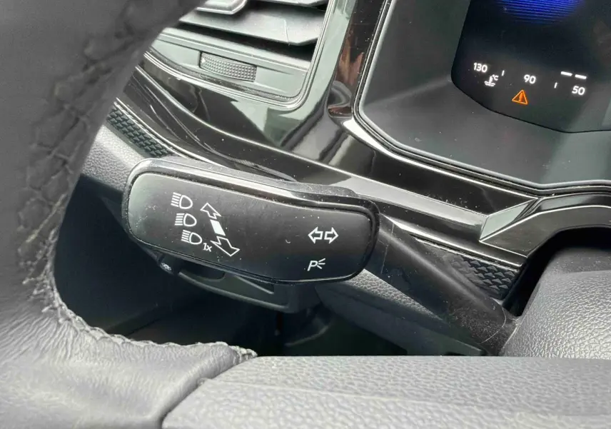 Gros plan sur la manette de clignotants noire et le combiné d'instruments digital dans l'habitacle d'une Volkswagen Polo grise.