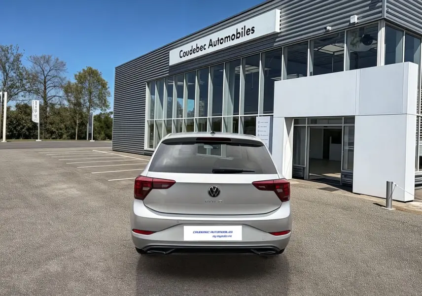Vue arrière d'une Volkswagen Polo grise 2025 stationnée devant un bâtiment moderne de concession automobile.