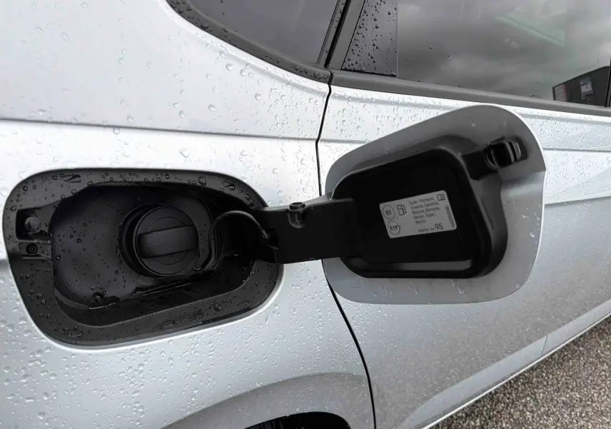 Gros plan sur la trappe à carburant ouverte côté gauche d'une Volkswagen Polo grise sous la pluie.