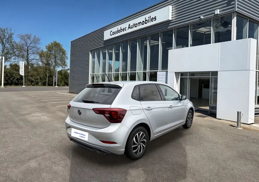 Volkswagen Polo grise vue 3/4 arrière droit, stationnée devant un bâtiment commercial moderne.