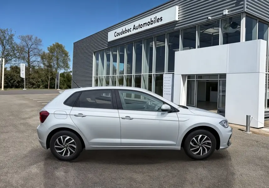 Vue de profil côté gauche d'une Volkswagen Polo grise 2025 stationnée devant un bâtiment commercial.