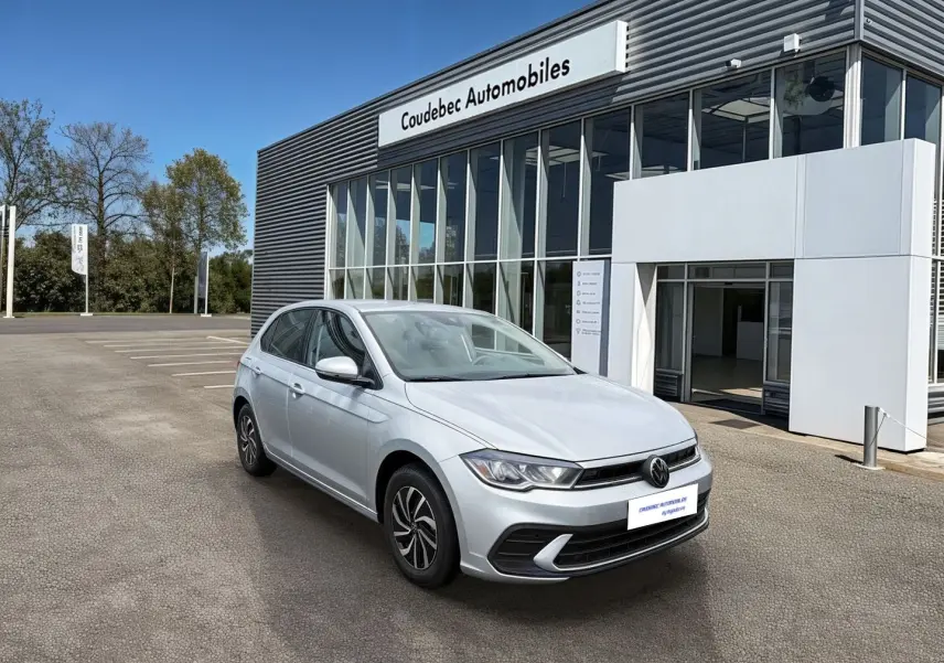 Volkswagen Polo grise vue 3/4 avant droit devant un bâtiment de concession automobile.