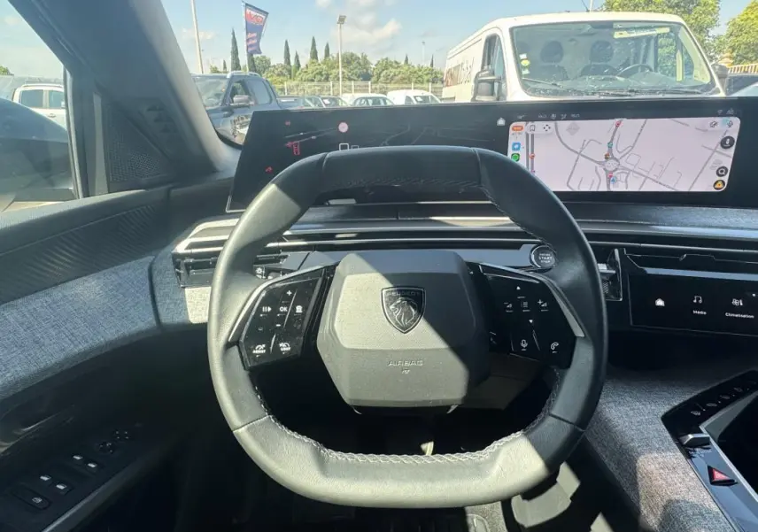 Vue intérieure centrée sur le volant compact du Peugeot 3008 Hybrid 2025 avec cockpit numérique et finition tissu gris.