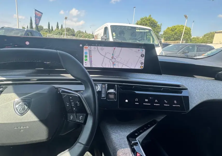 Vue intérieure du tableau de bord du Peugeot 3008 Hybrid 2025, avec volant noir et écran tactile central affichant la navigation.