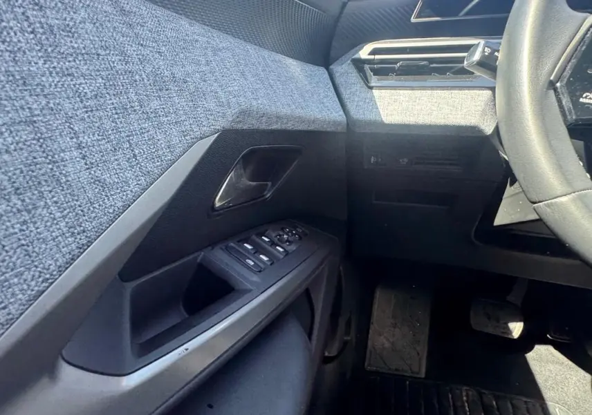 Vue intérieure côté gauche du Peugeot 3008 Hybrid 136 e-DCS6 Allure 2025, montrant la portière avec commandes et tissu gris.