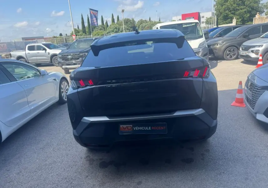 Vue arrière d’un Peugeot 3008 Hybrid gris foncé avec feux arrière allumés, garé parmi d’autres véhicules.