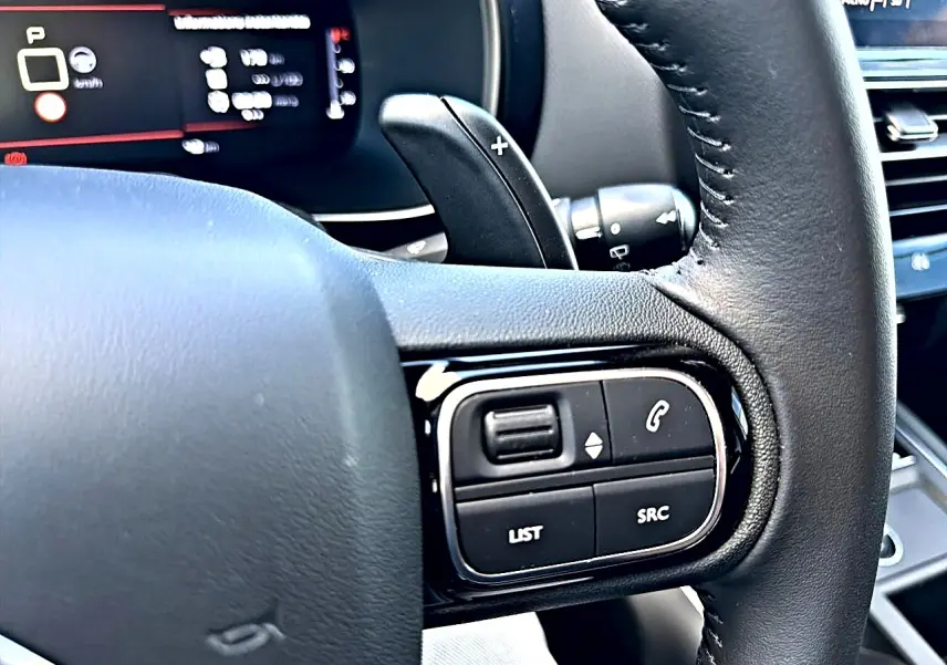 Gros plan sur le volant cuir noir côté gauche du Citroën C5 Aircross 2025 avec commandes multifonctions et palettes de boîte auto.