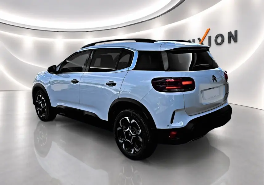Vue 3/4 arrière droite du Citroën C5 Aircross blanc avec jantes noires et vitres arrière teintées dans un showroom.