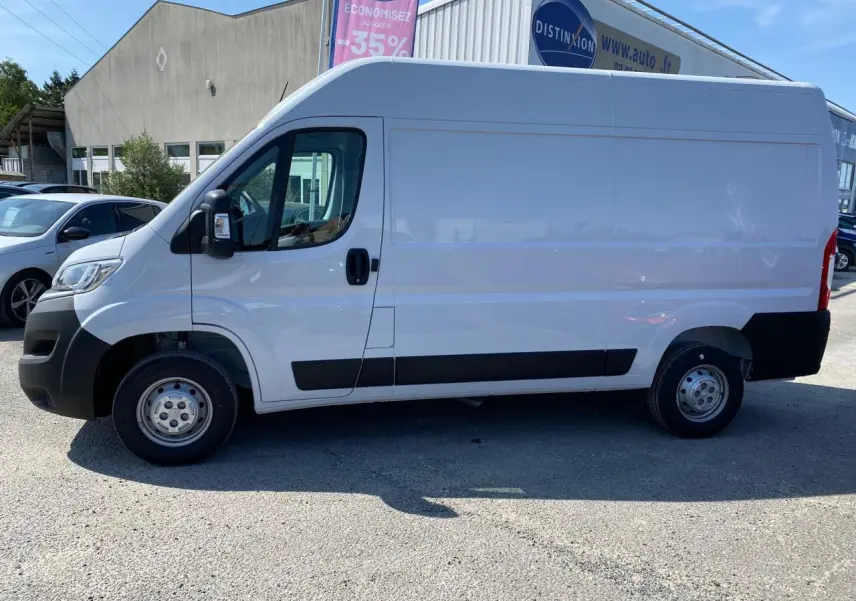 Vue de profil côté gauche d'un utilitaire Citroën Jumper blanc 2023 avec portes avant tôlées et roue de secours visible.